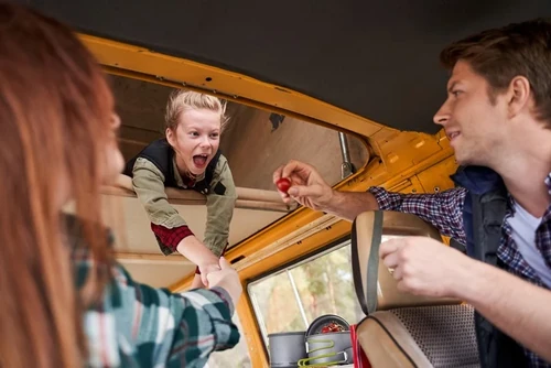 A young blonde girl in an RV is delighted to be given a cherry tomato by her father.