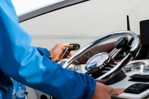 A close-up of a man’s hands on the steering wheel of a motor boat.