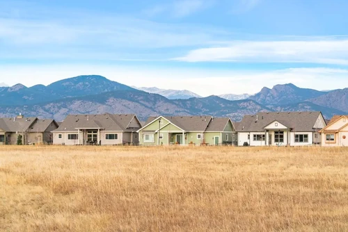 A row of houses in Loveland, CO, with a grass field and scenic Rocky Mountains.