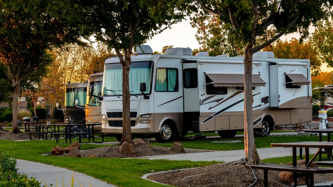 RV parked in a park with green grass and trees surrounding. 