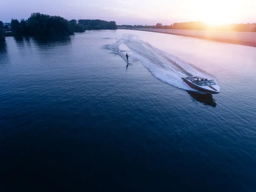 A man water skiing on a lake behind a boat at sunset.
