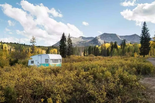 A camper parked amid autumn foliage with Colorado mountains looming.